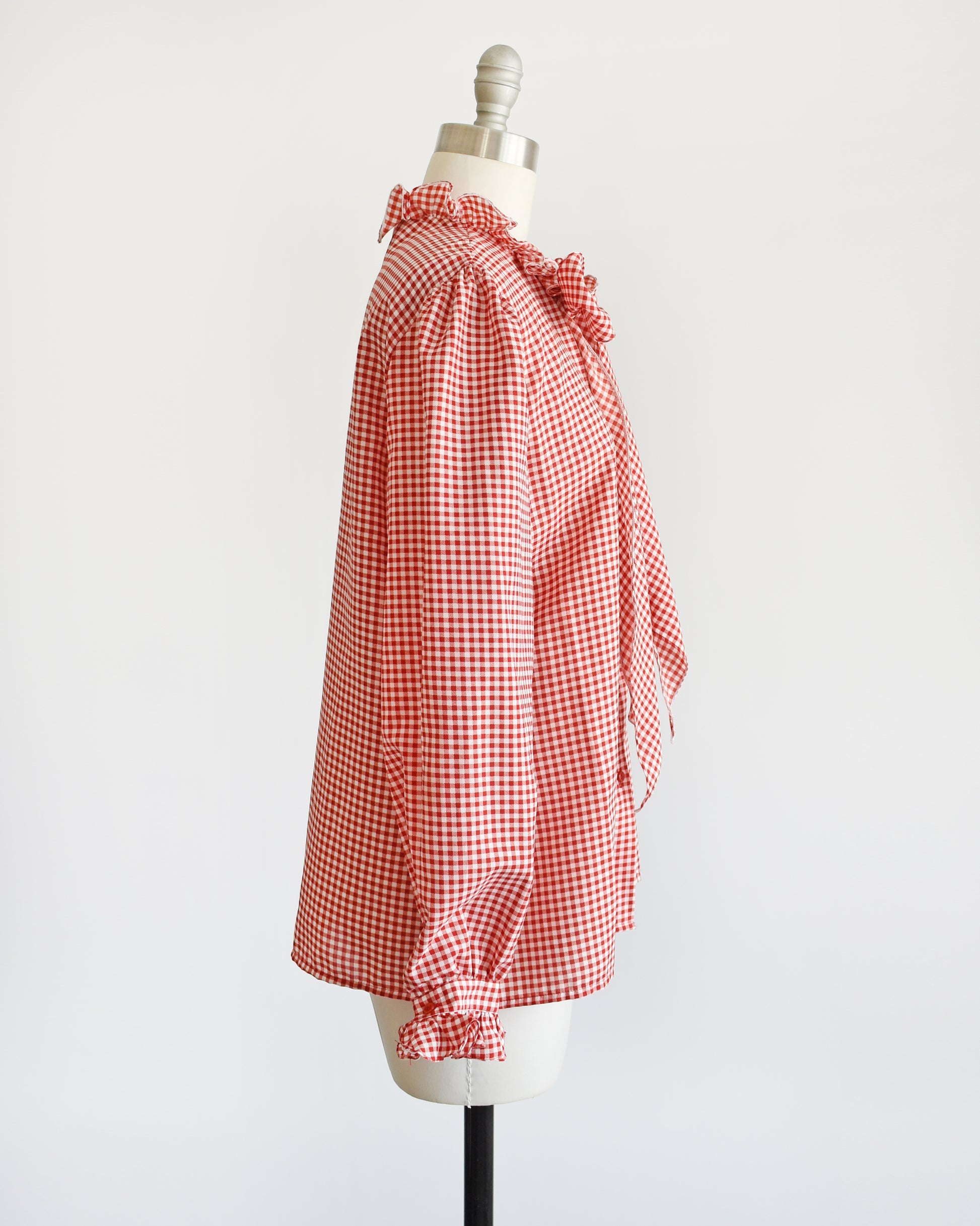 Side view of a vintage 1980s red and white gingham blouse with ruffled collar and ascot bow