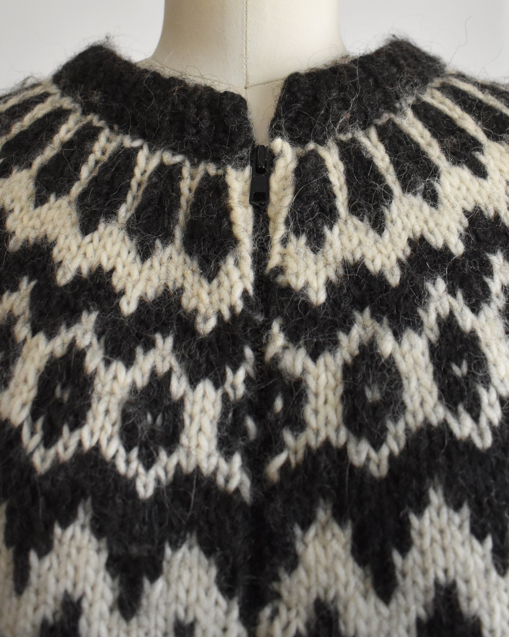 close up of the collar and zipper of a vintage black and white Fair Isle patterned sweater on a mannequin against a white background