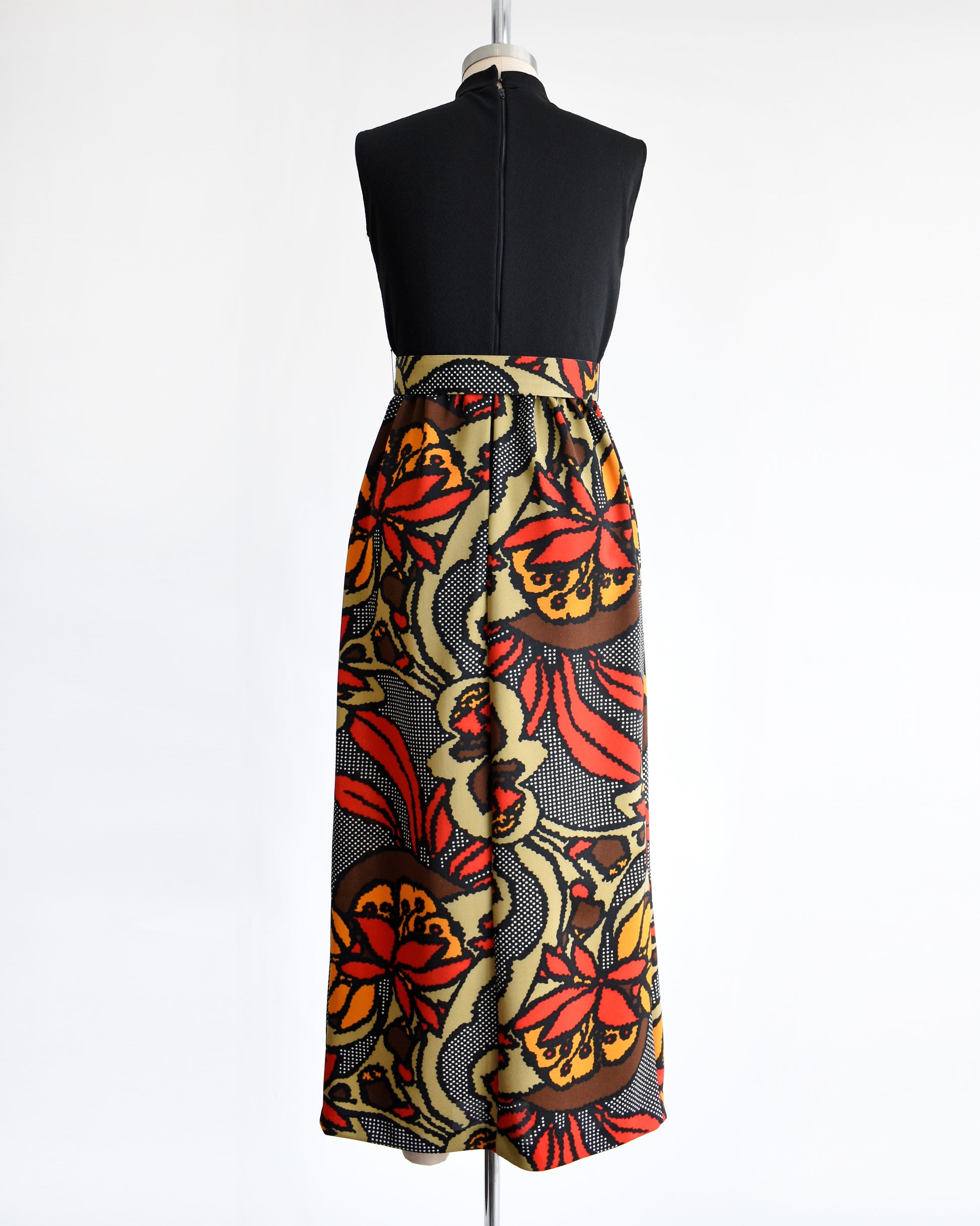 back view of a vintage 1970s maxi dress with a black bodice and a colorful bold floral print skirt with matching belt.