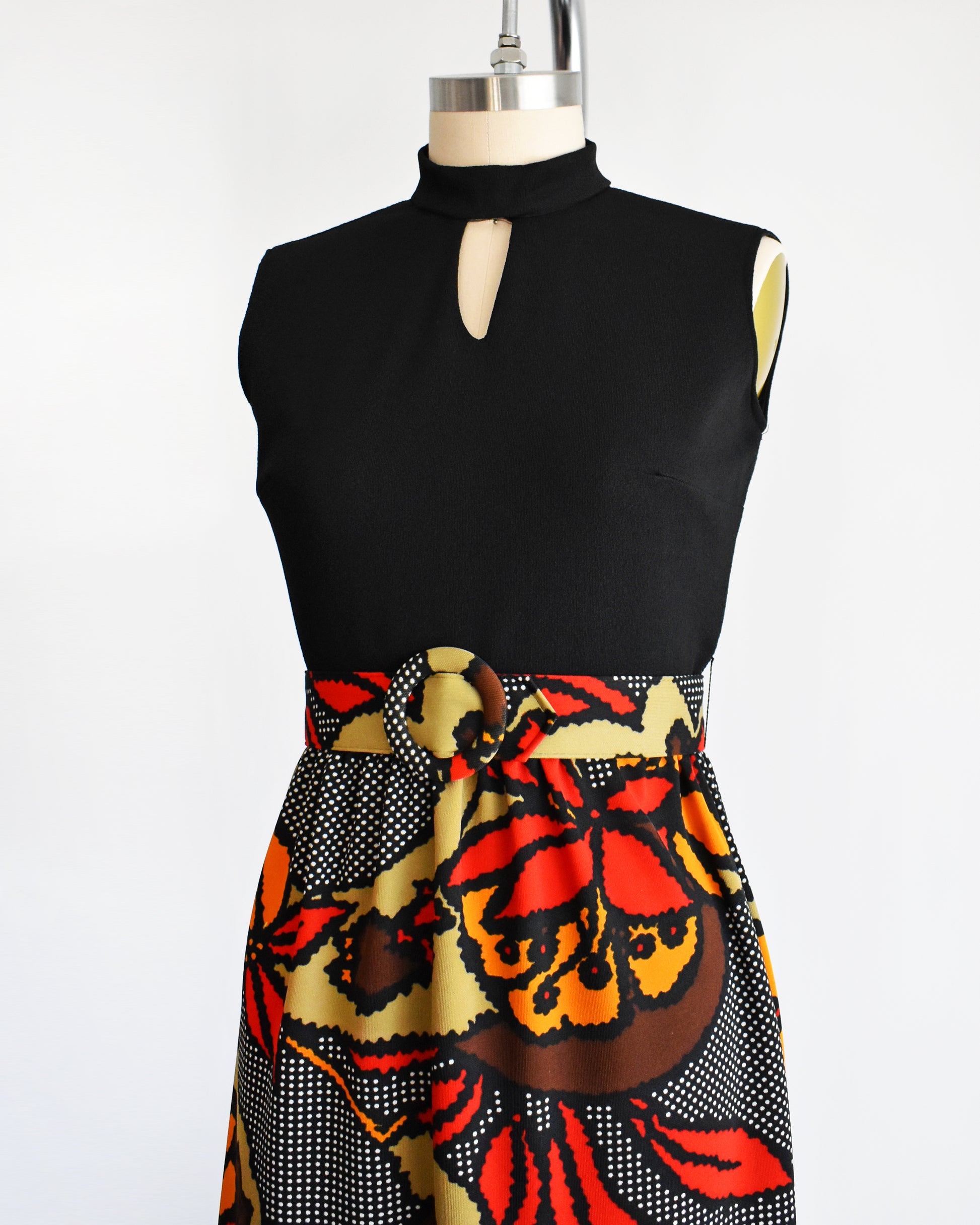 side front view of a vintage 1970s maxi dress with a black bodice and a colorful bold floral print skirt with matching belt.