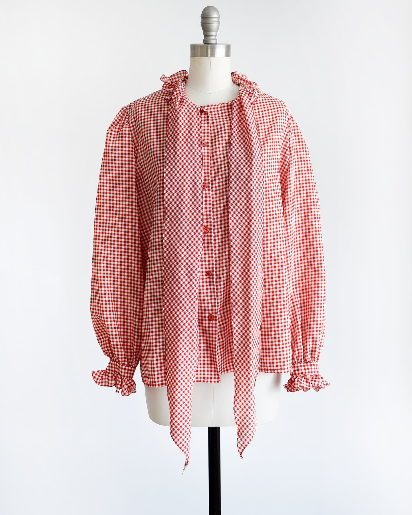 A vintage 1980s red and white gingham blouse with ruffled collar and ascot bow that is untied in this photo