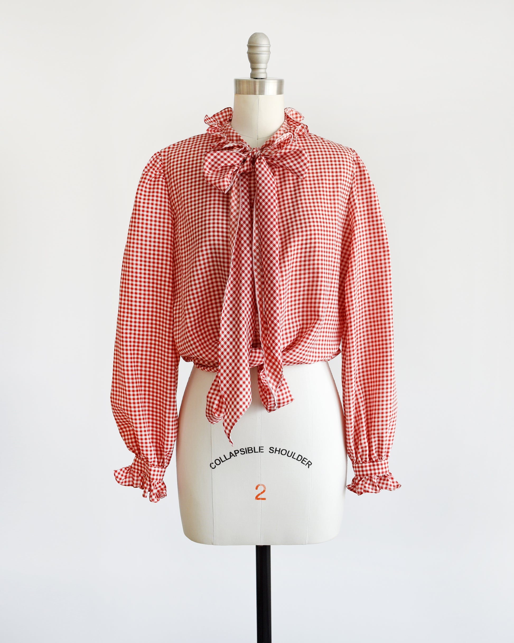 A vintage 1980s red and white gingham blouse with ruffled collar and ascot bow. The blouse is tied at the bottom giving it a cropped look