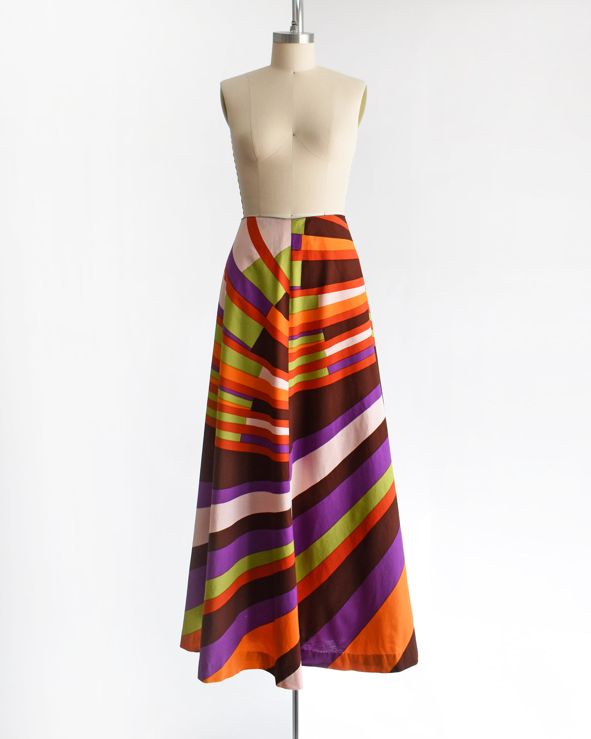 A high-waisted, vintage 1974 Marimekko A-line midi skirt with a bold retro diagonal stripe pattern in orange, purple, brown, green, and cream, displayed on a mannequin against a white background.
