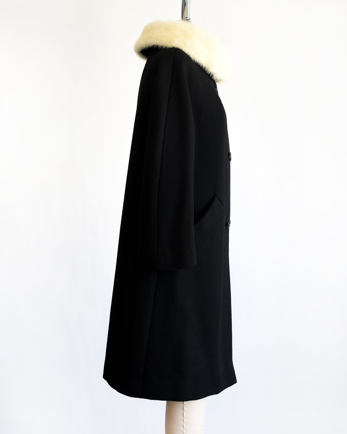 side view of a vintage 1960s Black coat with fur collar on a mannequin against a white background