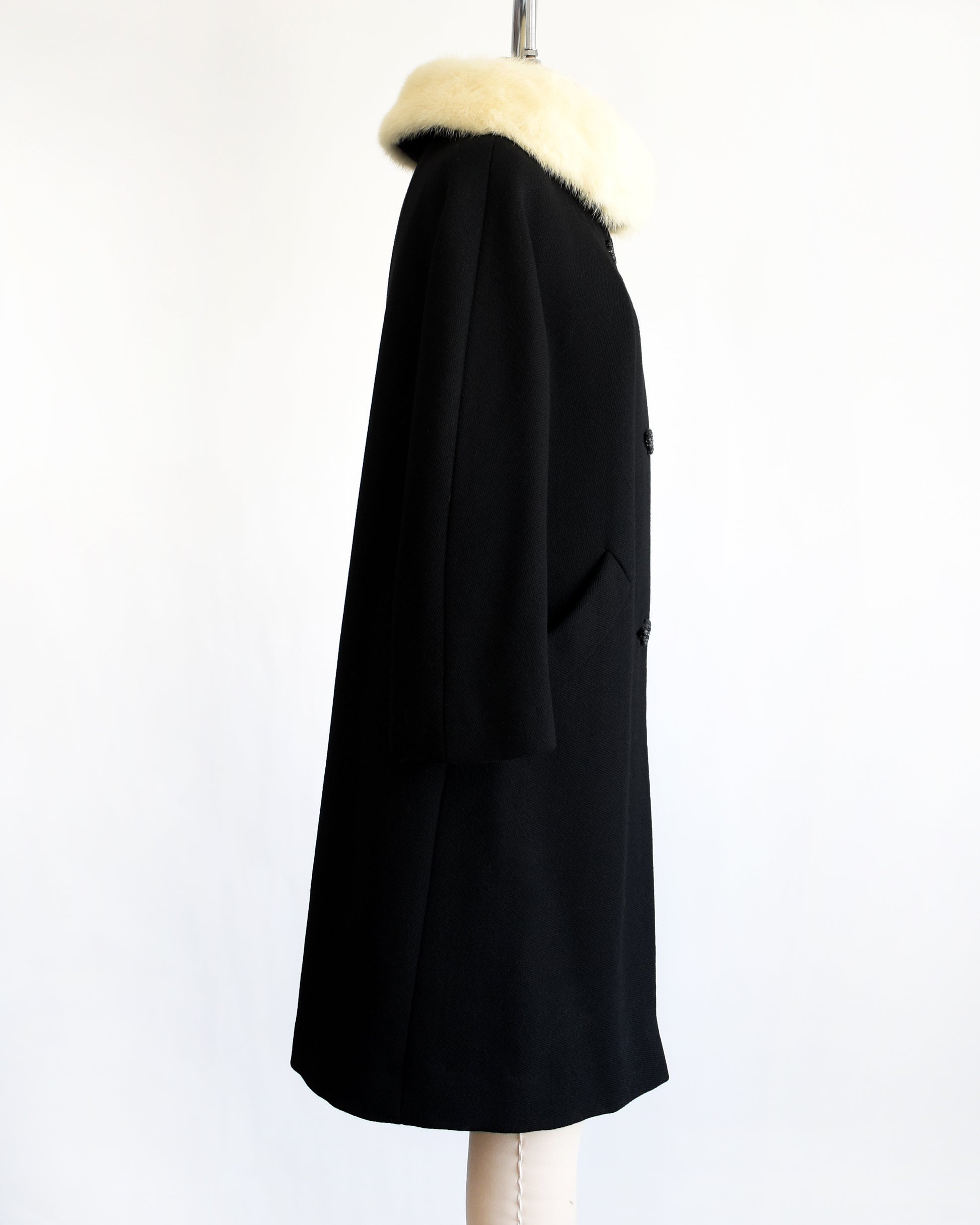 side view of a vintage 1960s Black coat with fur collar on a mannequin against a white background