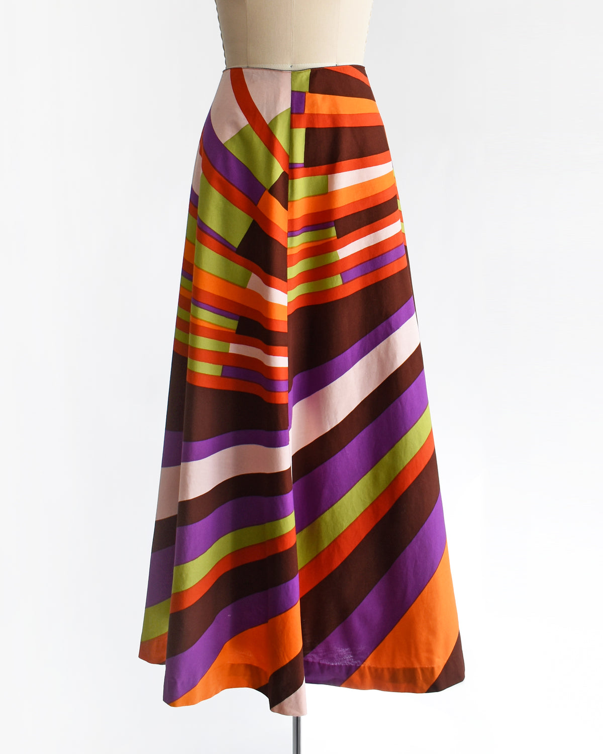 A high-waisted, vintage 1974 Marimekko A-line midi skirt with a bold retro diagonal stripe pattern in orange, purple, brown, green, and cream, displayed on a mannequin against a white background.