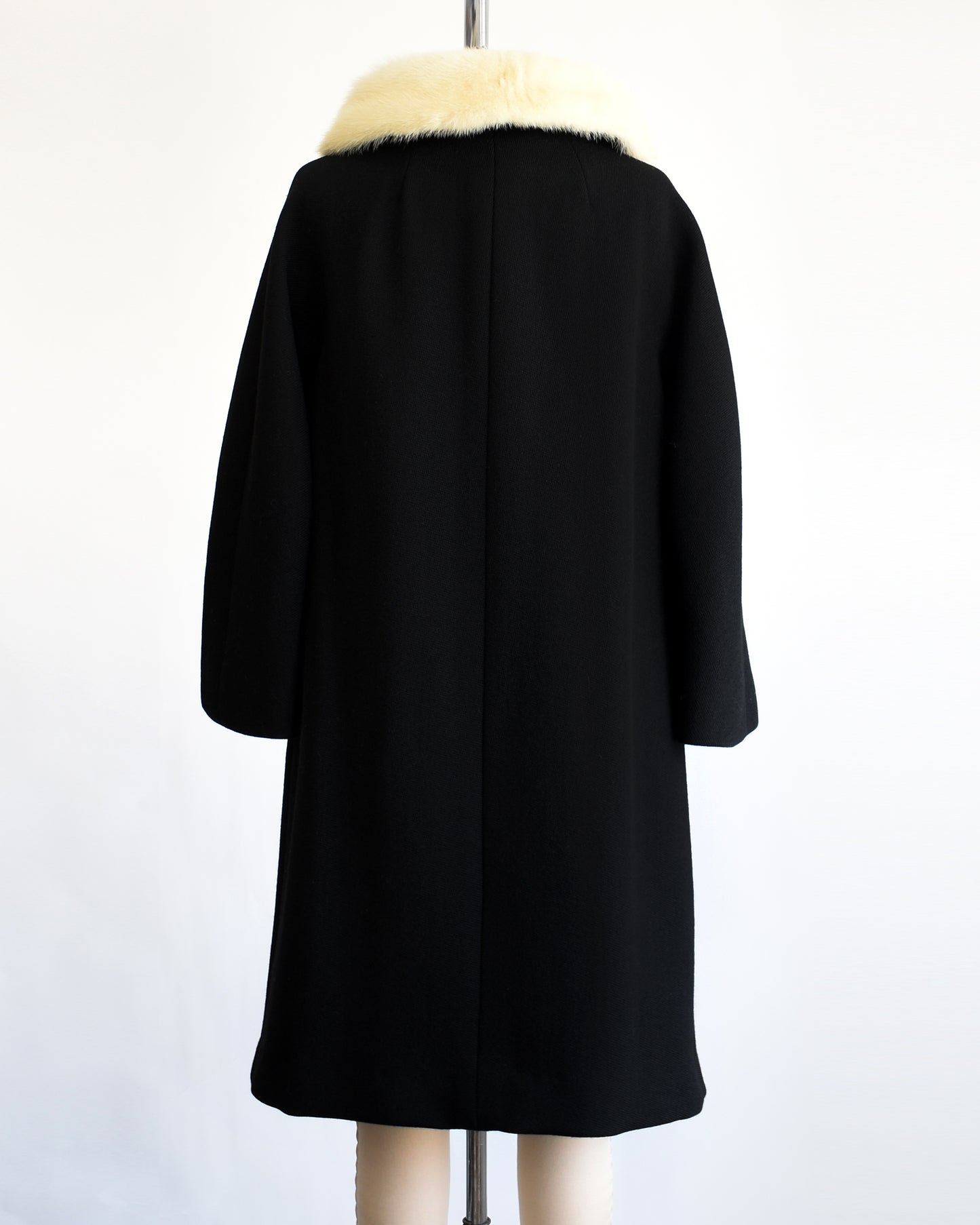 back view of a vintage 1960s Black coat with fur collar on a mannequin against a white background