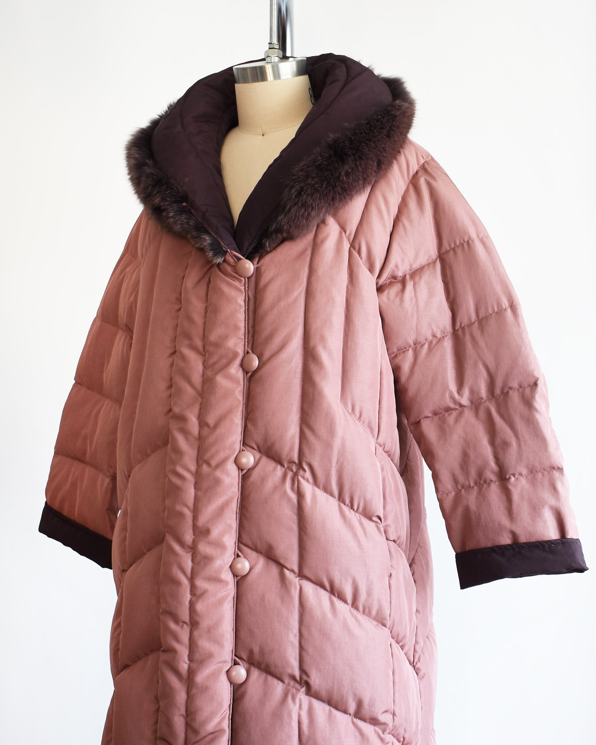 side front view of a vintage 1980s quilted puffer reversible coat with purple faux fur trim. this shows the mauve side of the coat.