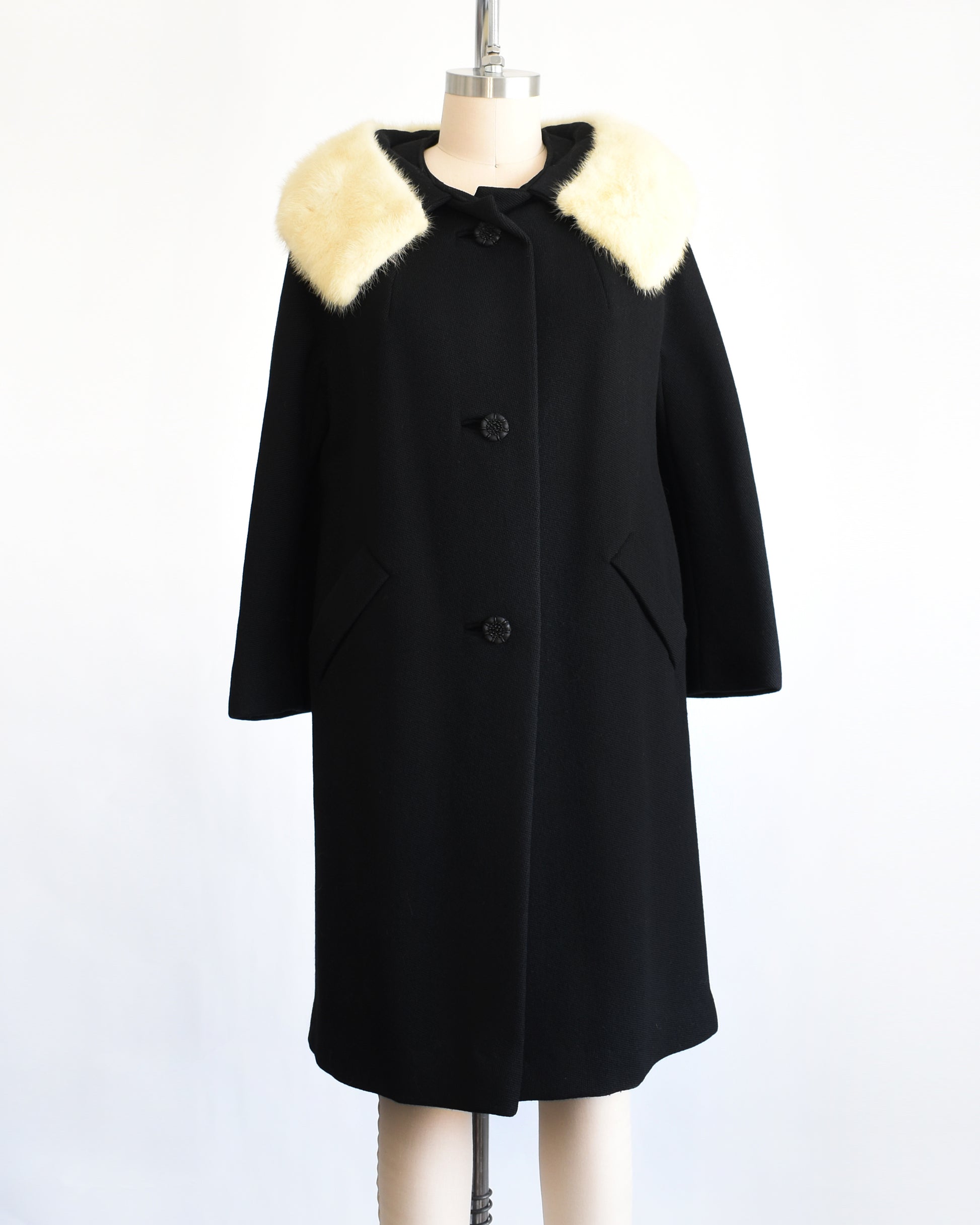 a vintage 1960s Black coat with fur collar on a mannequin against a white background. The collar is unbuttoned in this photo