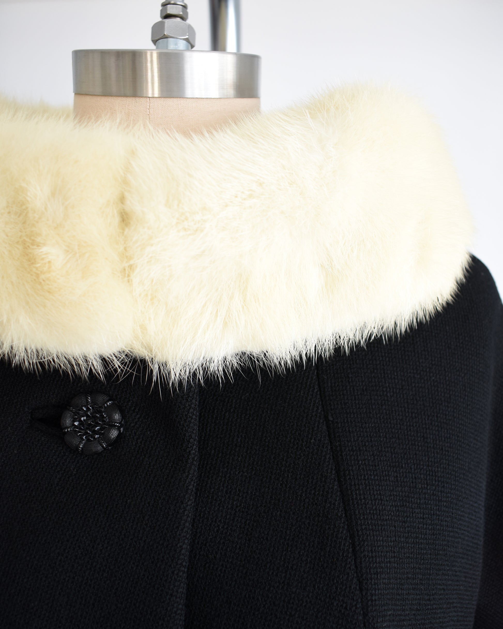 close up of a vintage 1960s Black coat with fur collar on a mannequin against a white background