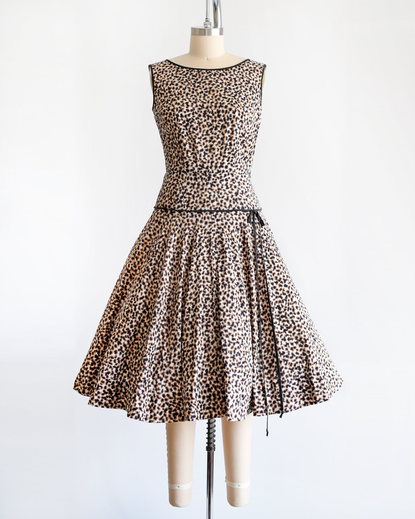 A vintage 1950s leopard print dress with black trim on a dress form.