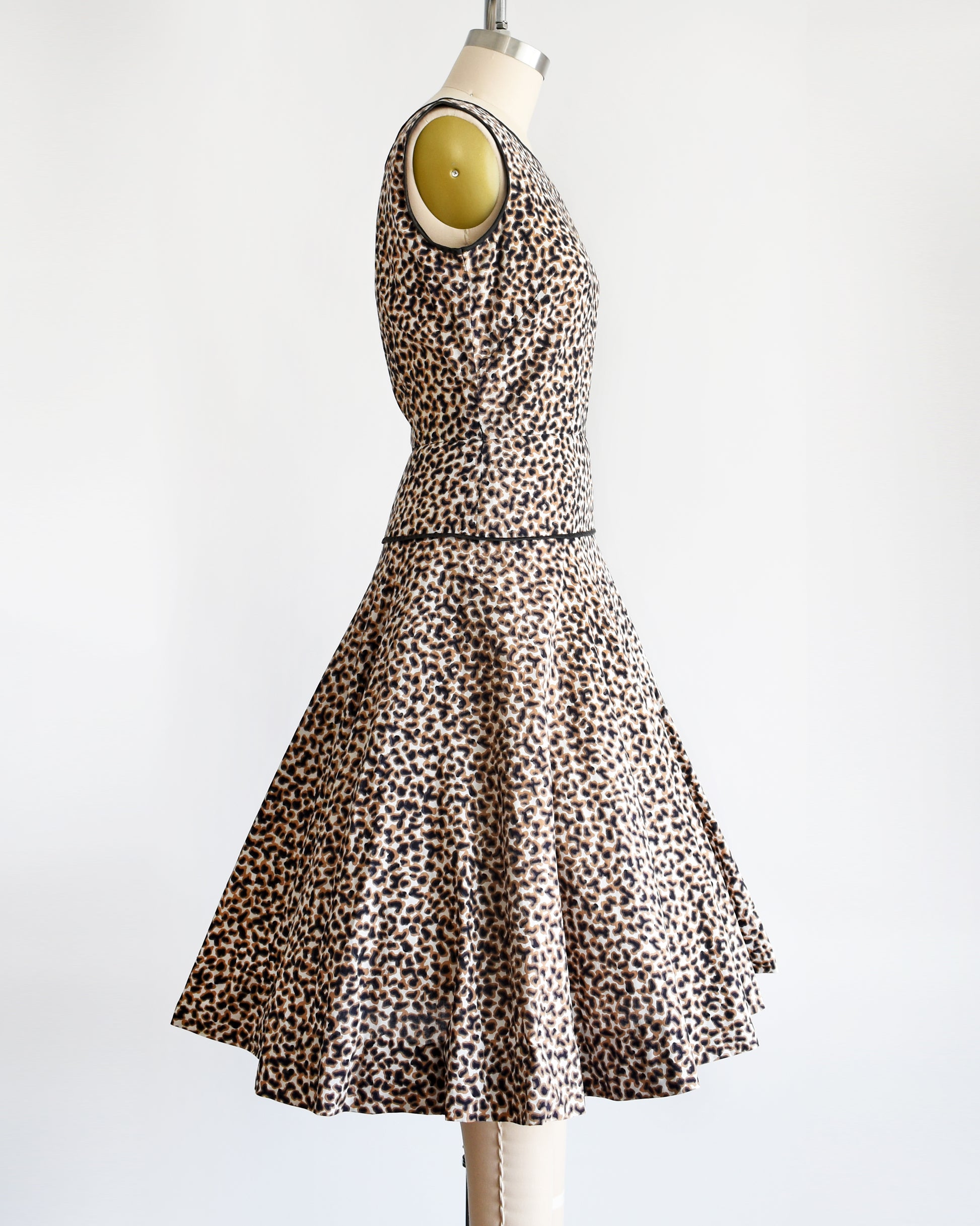 Side view of a vintage 1950s leopard print dress with black trim on a dress form.
