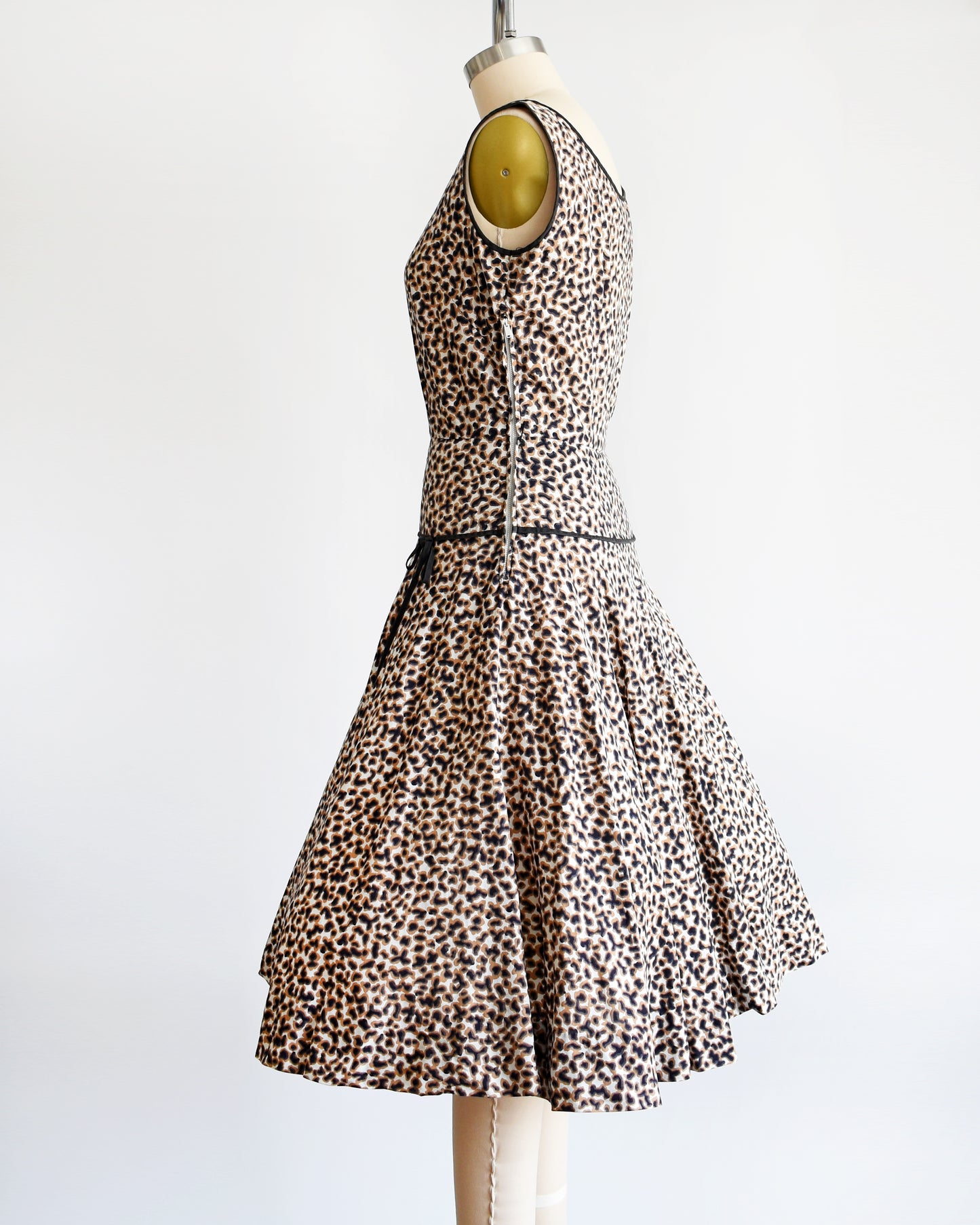 Side view of a vintage 1950s leopard print dress with black trim on a dress form. There is a zipper on the side.