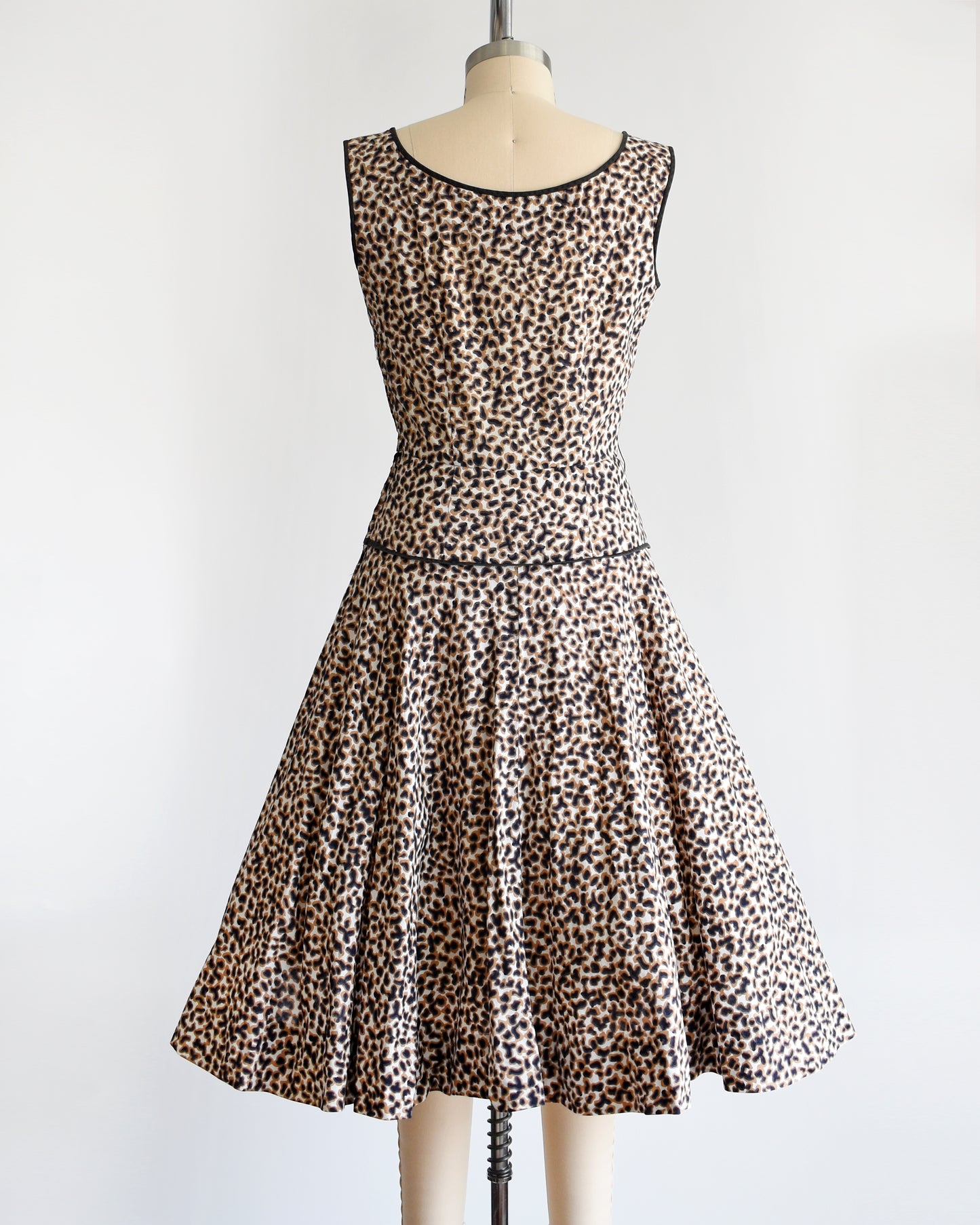 Back view of a vintage 1950s leopard print dress with black trim on a dress form.