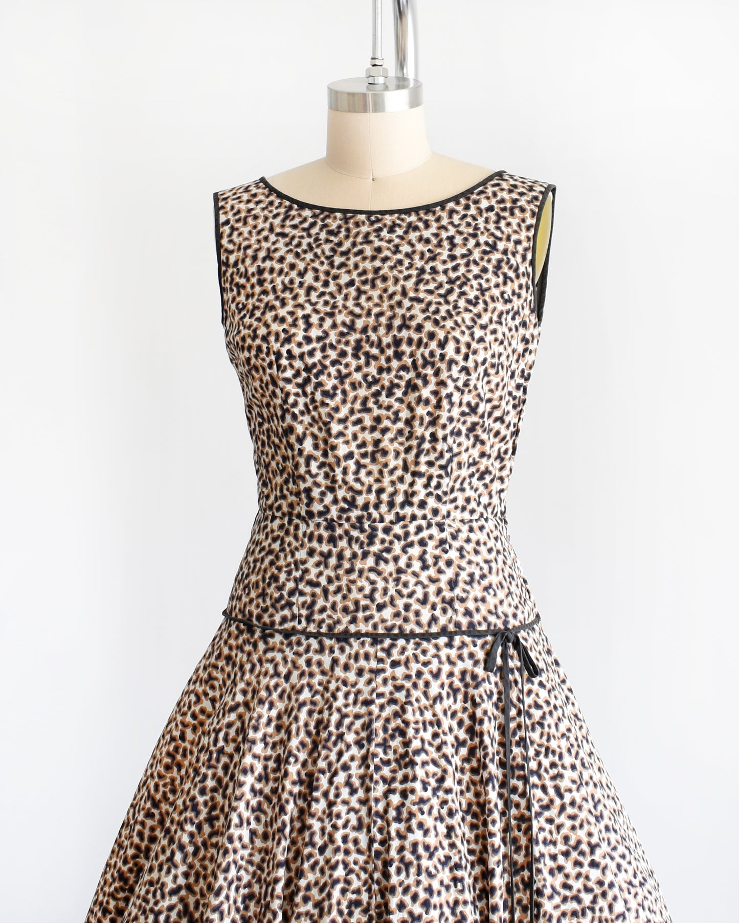 Side front view of a vintage 1950s leopard print dress with black trim on a dress form.