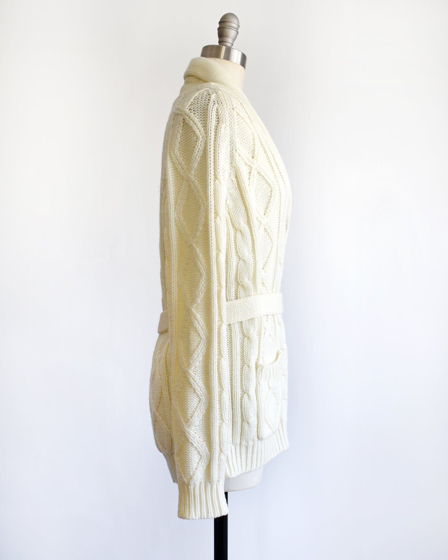 side view of a vintage 1980s cream cable knit cardigan with faux wood buttons and matching tie belt