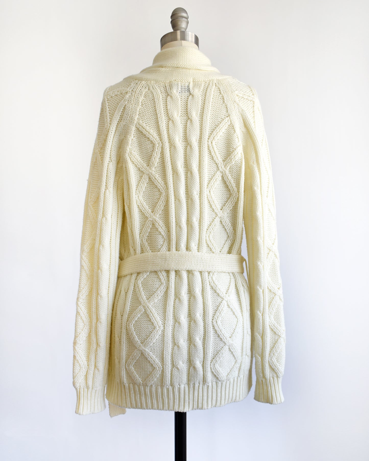 back view of a vintage 1980s cream cable knit cardigan with faux wood buttons and matching tie belt