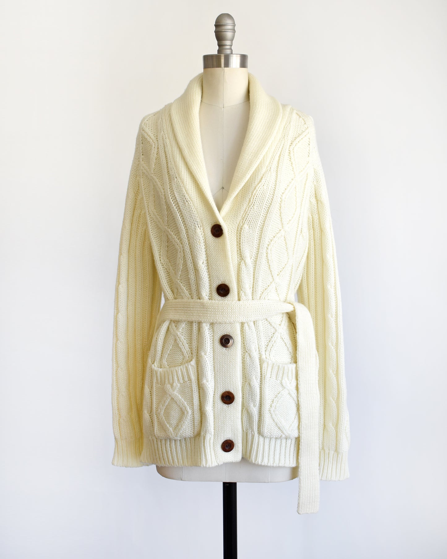 side front view of a vintage 1980s cream cable knit cardigan with faux wood buttons and matching tie belt