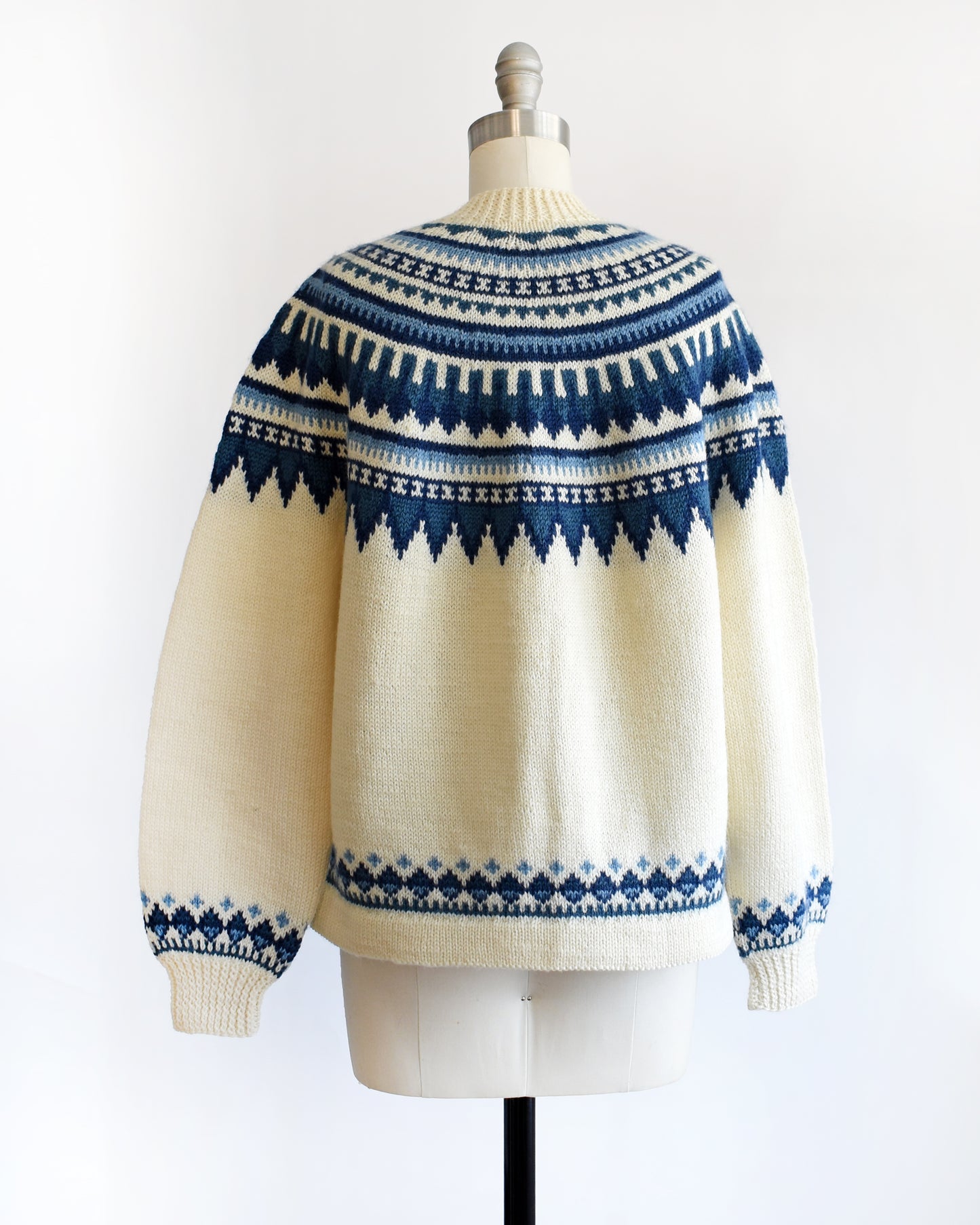back view of a vintage 1970s Cream-colored Fair Isle sweater with blue and white pattern on a mannequin against a white background