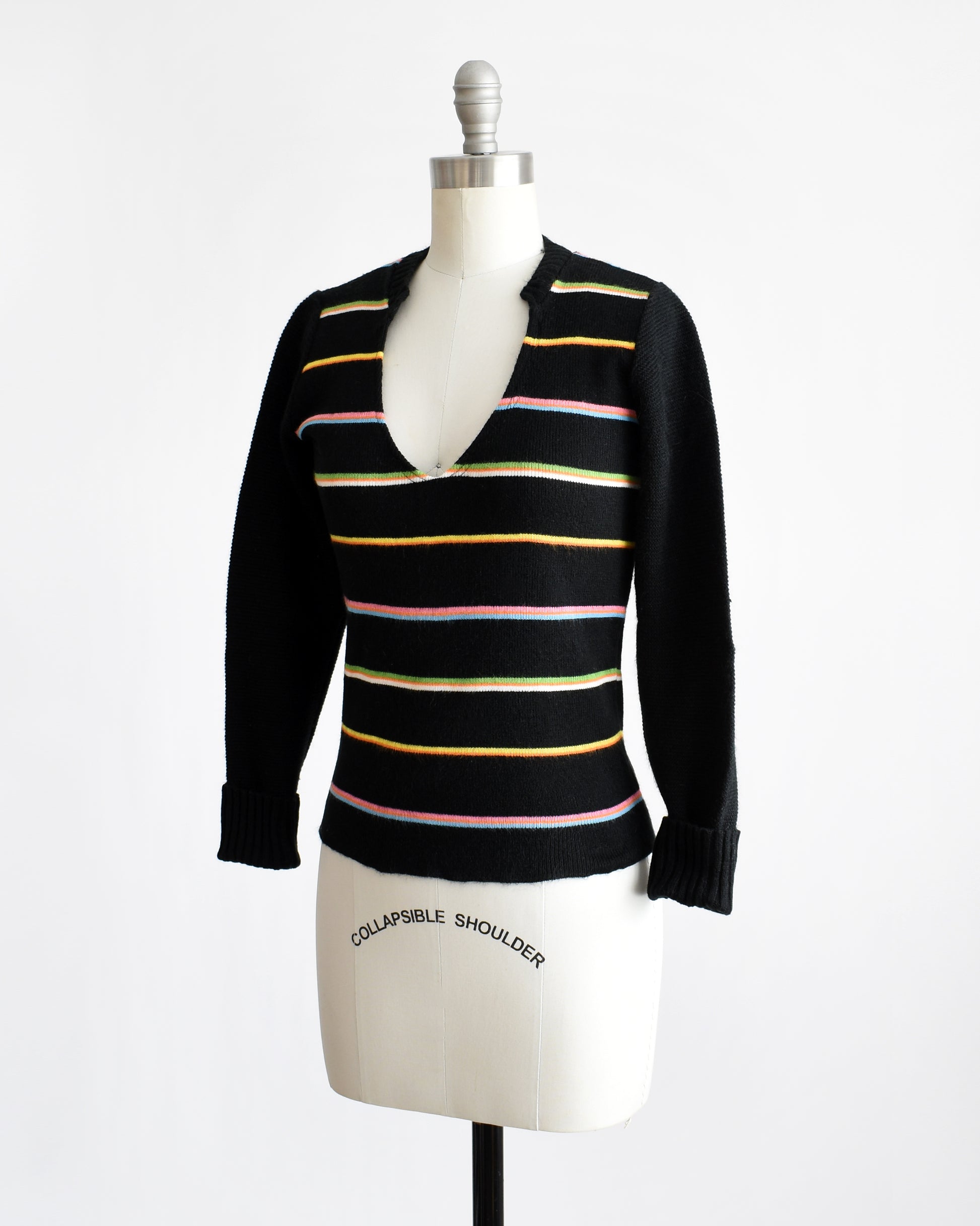 Side front view of a vintage 1970s sweater that features black knit with horizontal rainbow stripes, a curved v-neckline, and long sleeves that can be cuffed.