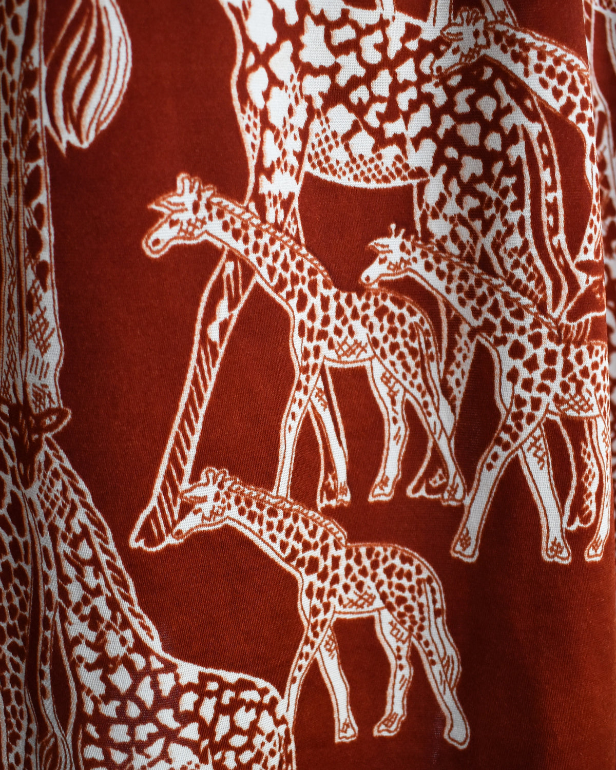 close up of a vintage 1970s long-sleeve A-line dress displayed on a mannequin against a plain white background. The dress features a rust-brown base with a white giraffe print and a keyhole neckline with button details.