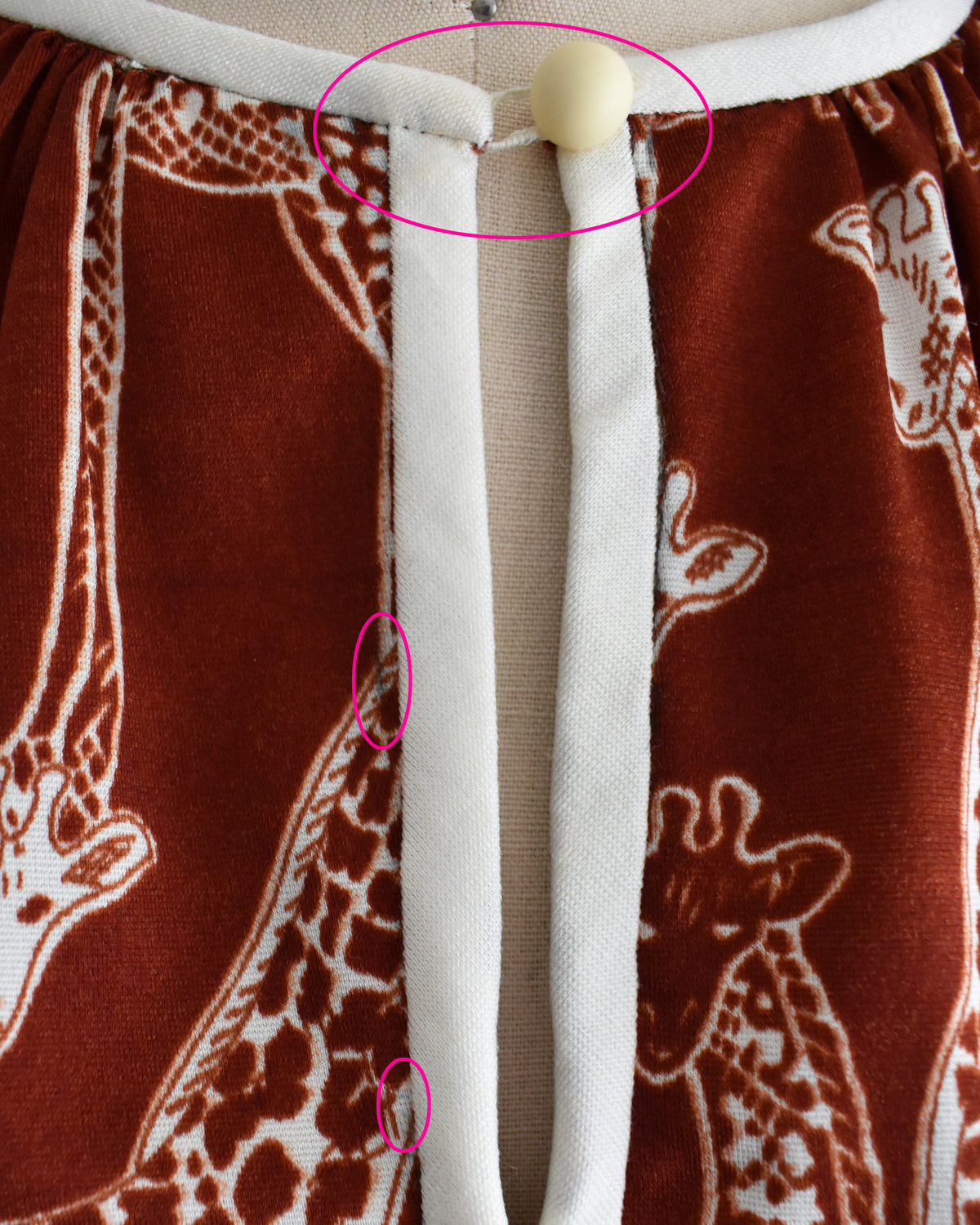 close up of the bodice on the dress, showing the stretched out loop on the keyhole button and some dark marks circled in pink