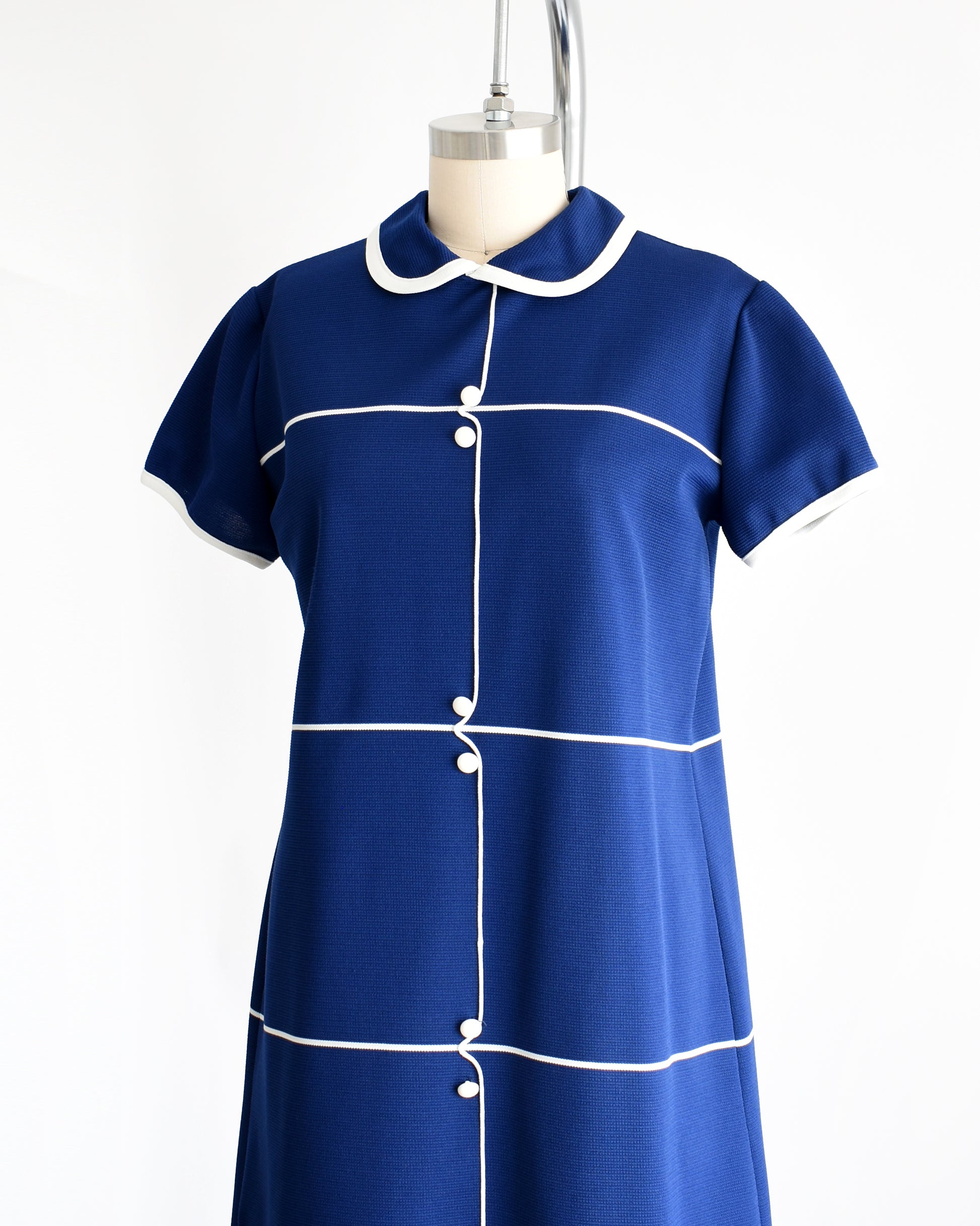 Side front view of a vintage 1960s navy blue dress with horizontal white stripes, along with a stripe down the front with decorative button accents.