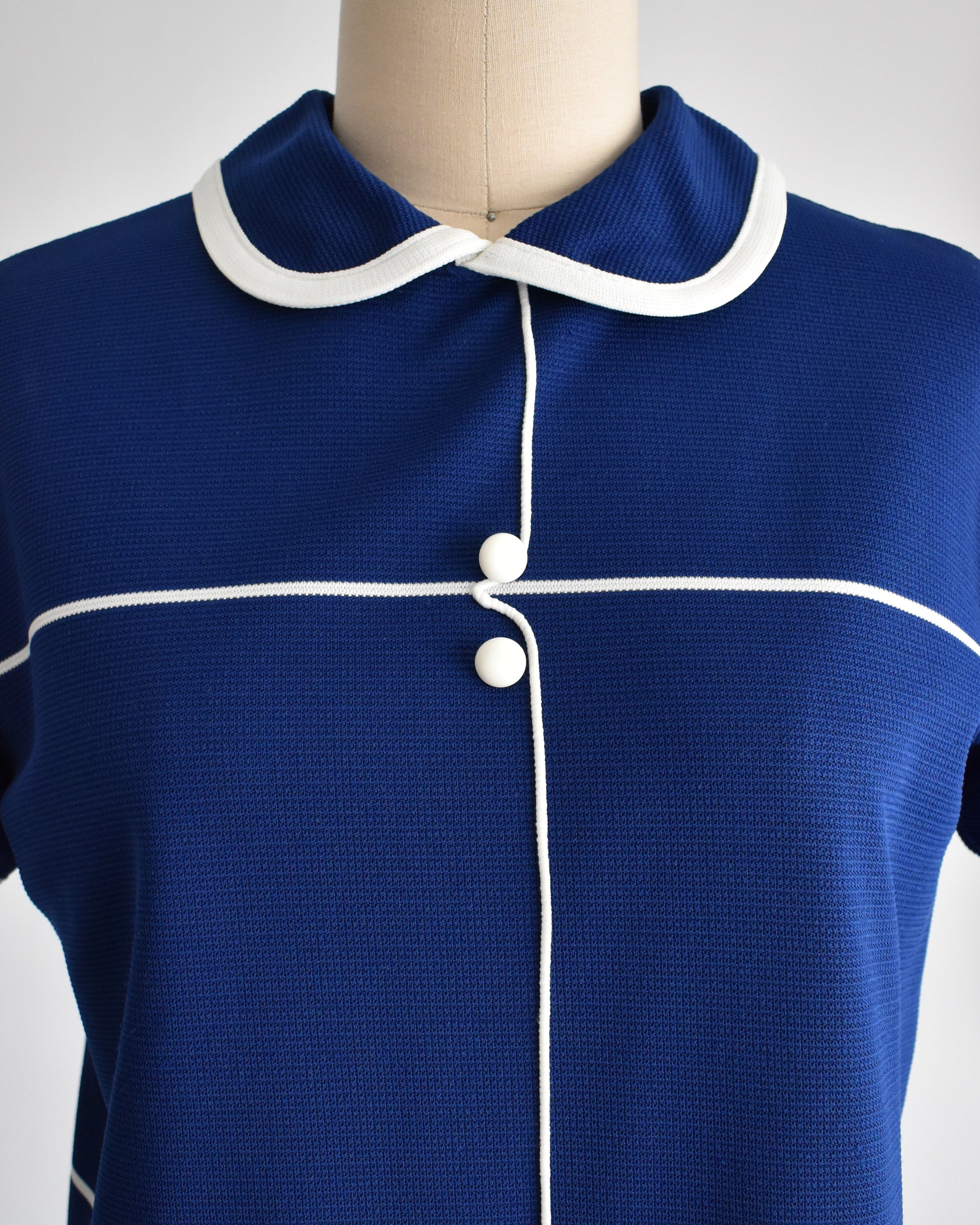 Close up of the navy blue knit, Peter Pan collar, white stripes, and button accents.