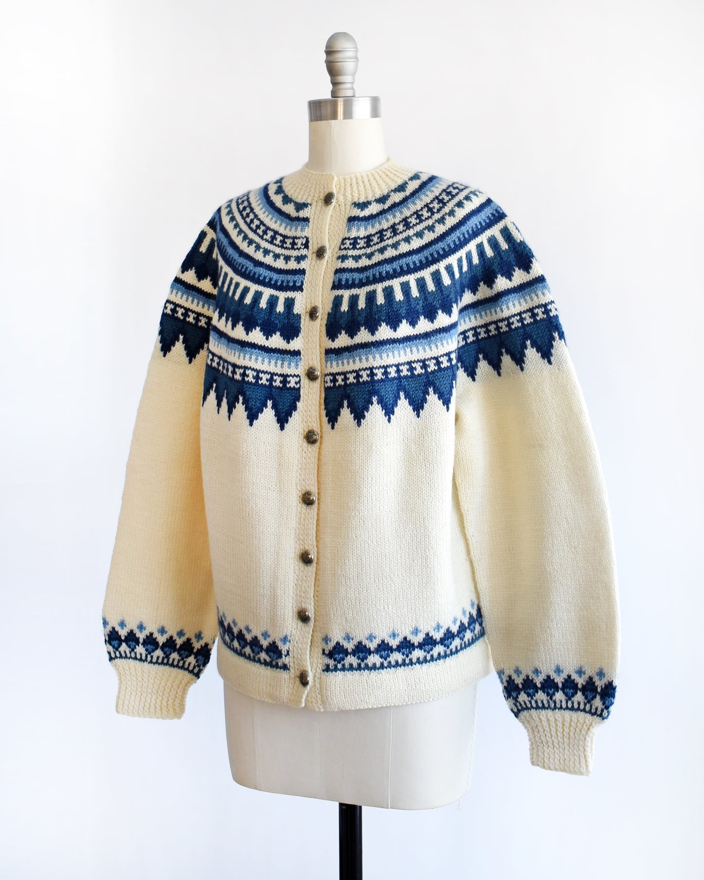 side front view of a vintage 1970s Cream-colored Fair Isle sweater with blue and white pattern on a mannequin against a white background