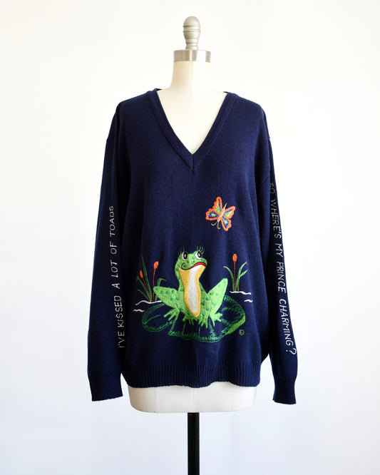 a vintage navy blue 1970s embroidered frog and butterfly sweater that says in white embroidery on the right sleeve "I Have Kissed A Lot Of Frogs," and the left sleeve has white embroidery "So Where Is My Prince Charming?"