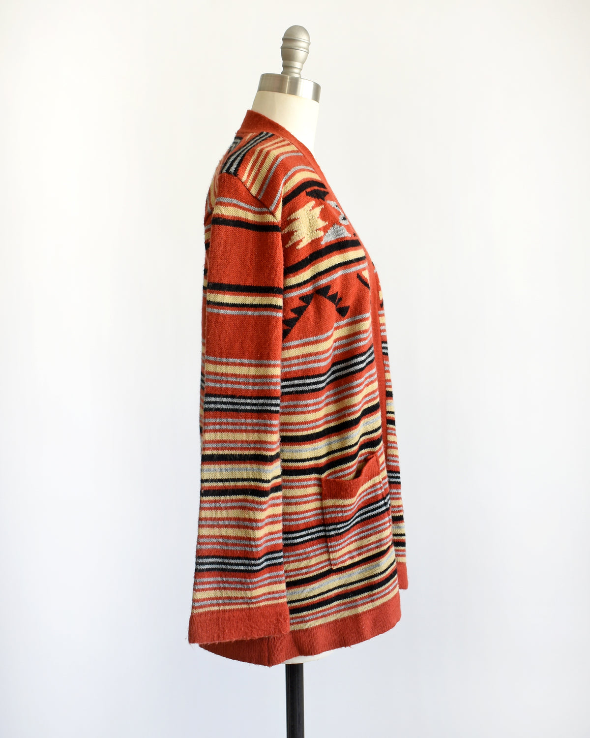 side view of a vintage 1970s long-sleeve open-front cardigan with a Southwestern geometric pattern, displayed on a white dress form mannequin against a plain white background.