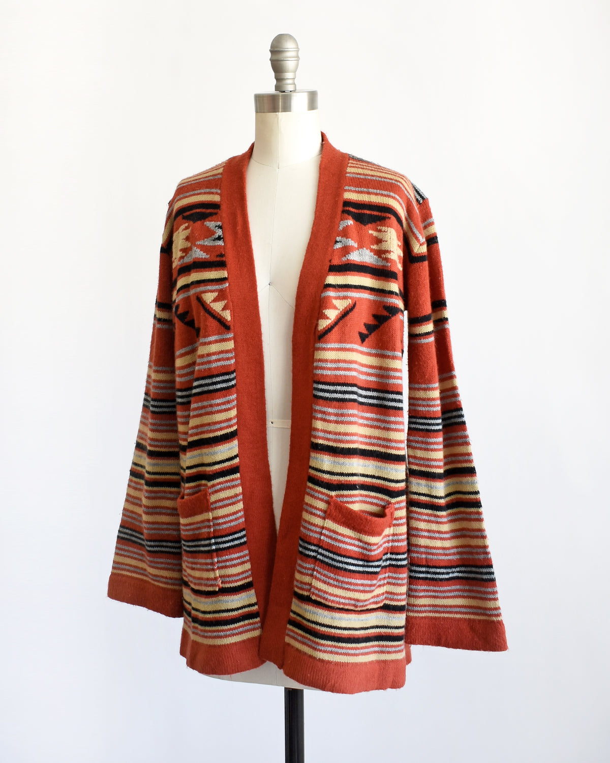 side front view of a vintage 1970s long-sleeve open-front cardigan with a Southwestern geometric pattern, displayed on a white dress form mannequin against a plain white background.