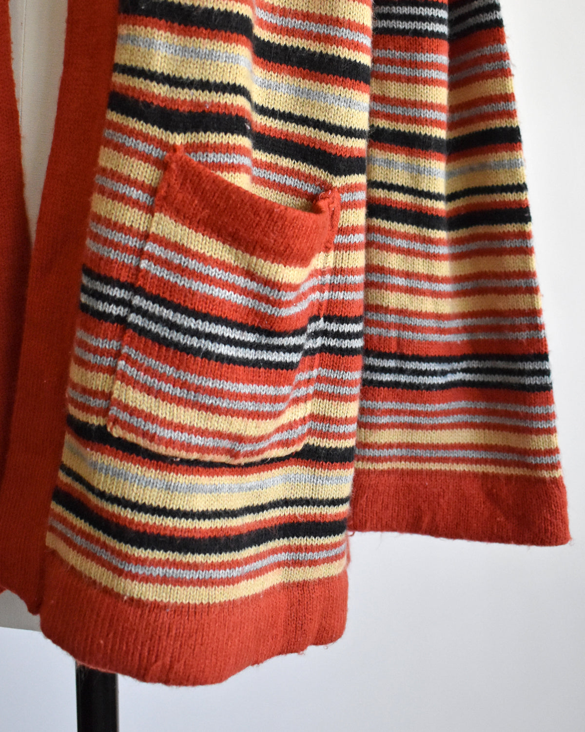 A close-up of  a vintage 1970s long-sleeve open-front cardigan with a Southwestern geometric pattern, displayed on a white dress form mannequin against a plain white background.