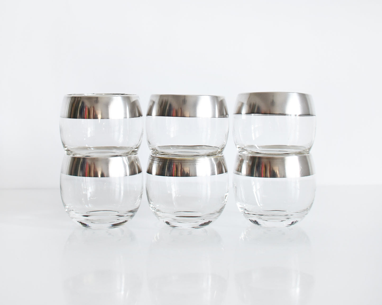 A row of three silver rim roly poly glasses that are stacked in twos on against a white background