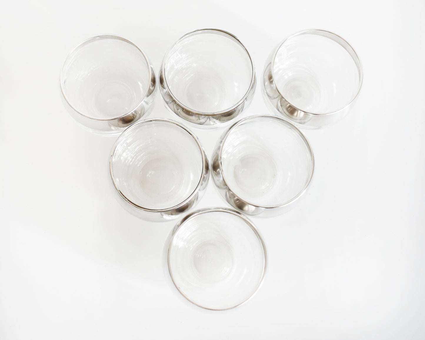 overhead shot of a six silver rim roly poly glasses that are round with flat bottoms against a white background