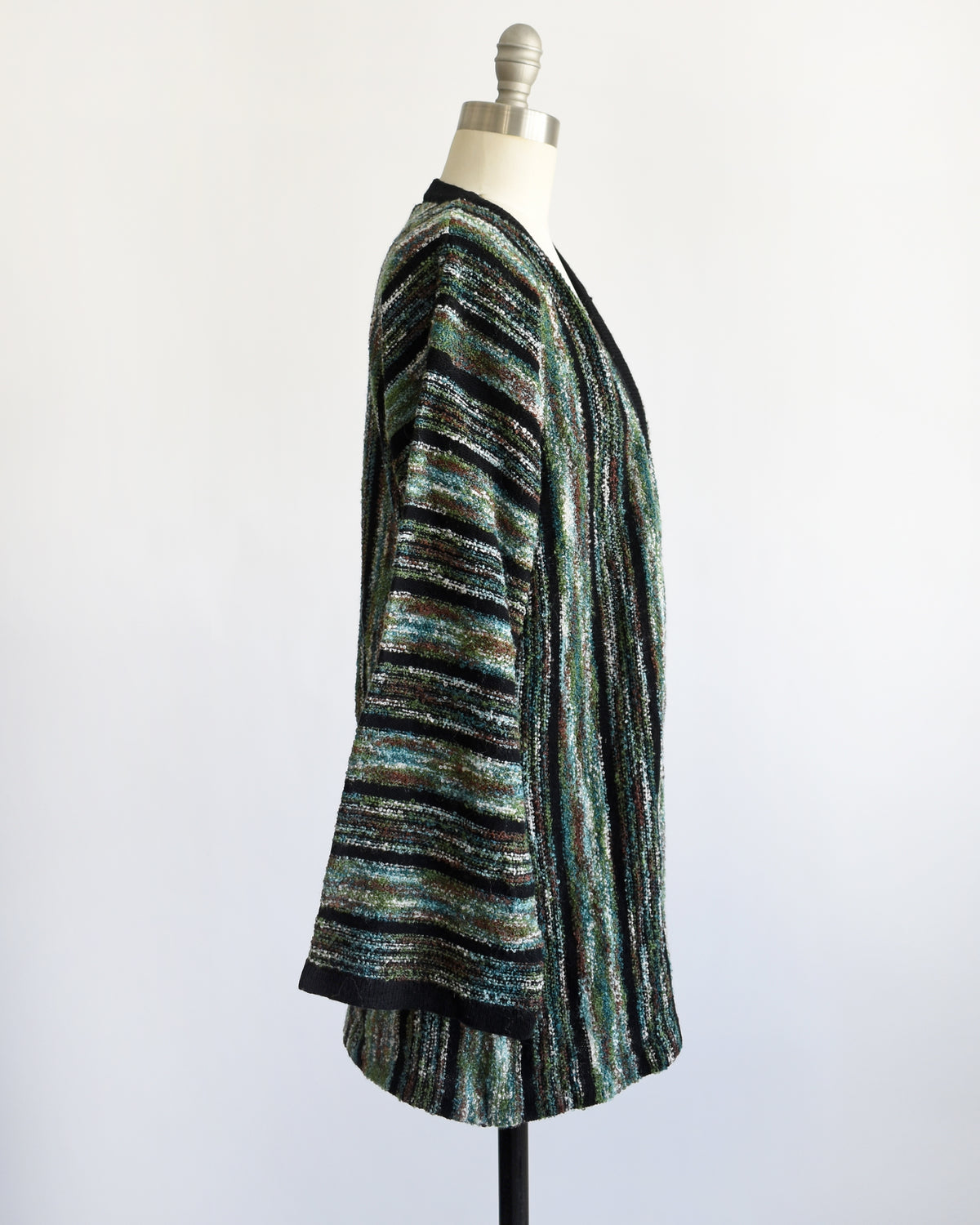 side view of A vintage 1970s open-front cardigan with wide bell sleeves, featuring a textured vertical stripe pattern in black, green, and white, displayed on a white dress form mannequin.