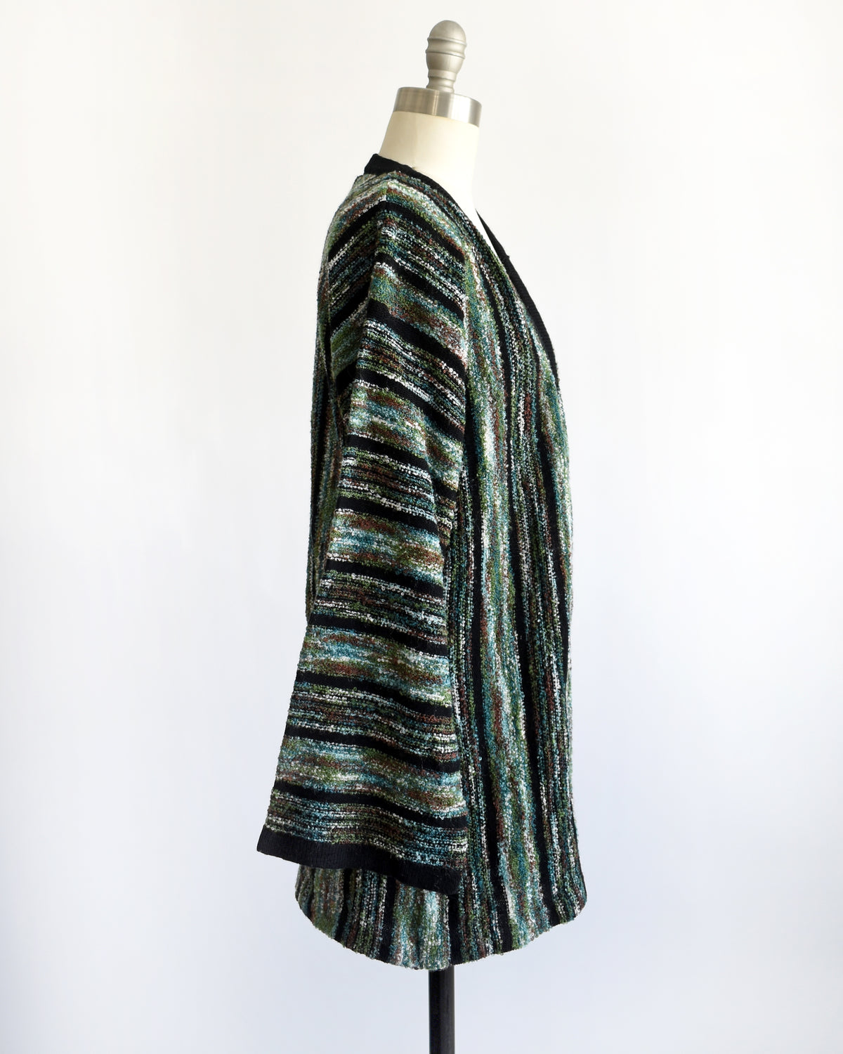 back view of a vintage 1970s open-front cardigan with wide bell sleeves, featuring a textured vertical stripe pattern in black, green, and white, displayed on a white dress form mannequin.