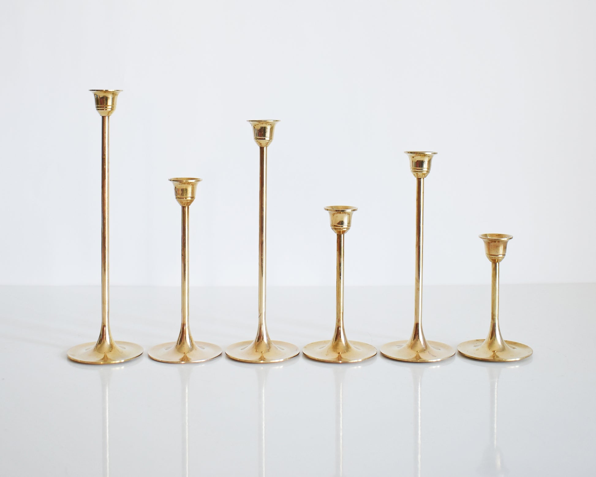 A set of six different vintage brass graduated candlesticks in a row. The row shows the different heights of the candlesticks