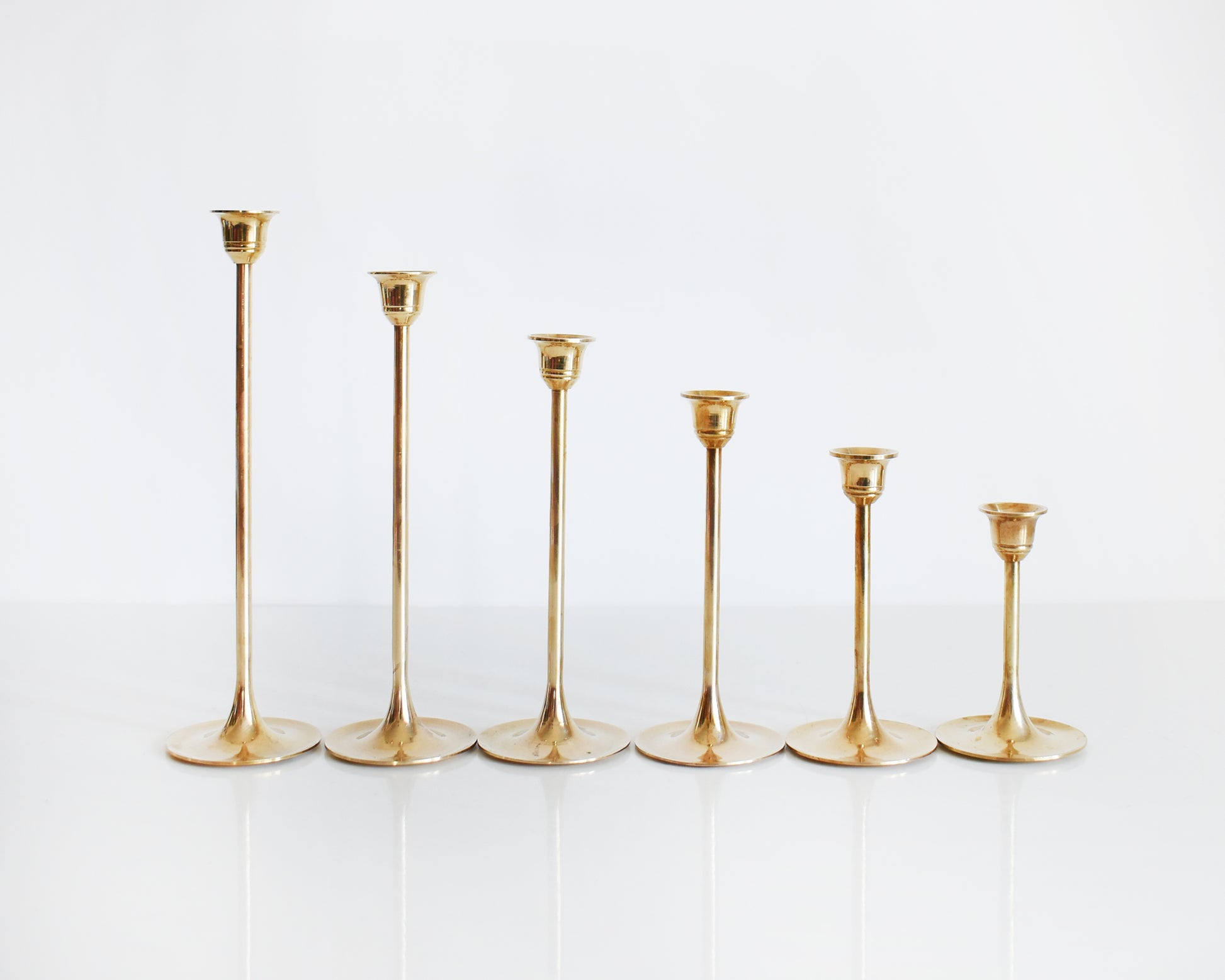 A set of six different vintage brass graduated candlesticks in a row. The row shows the different heights of the candlesticks