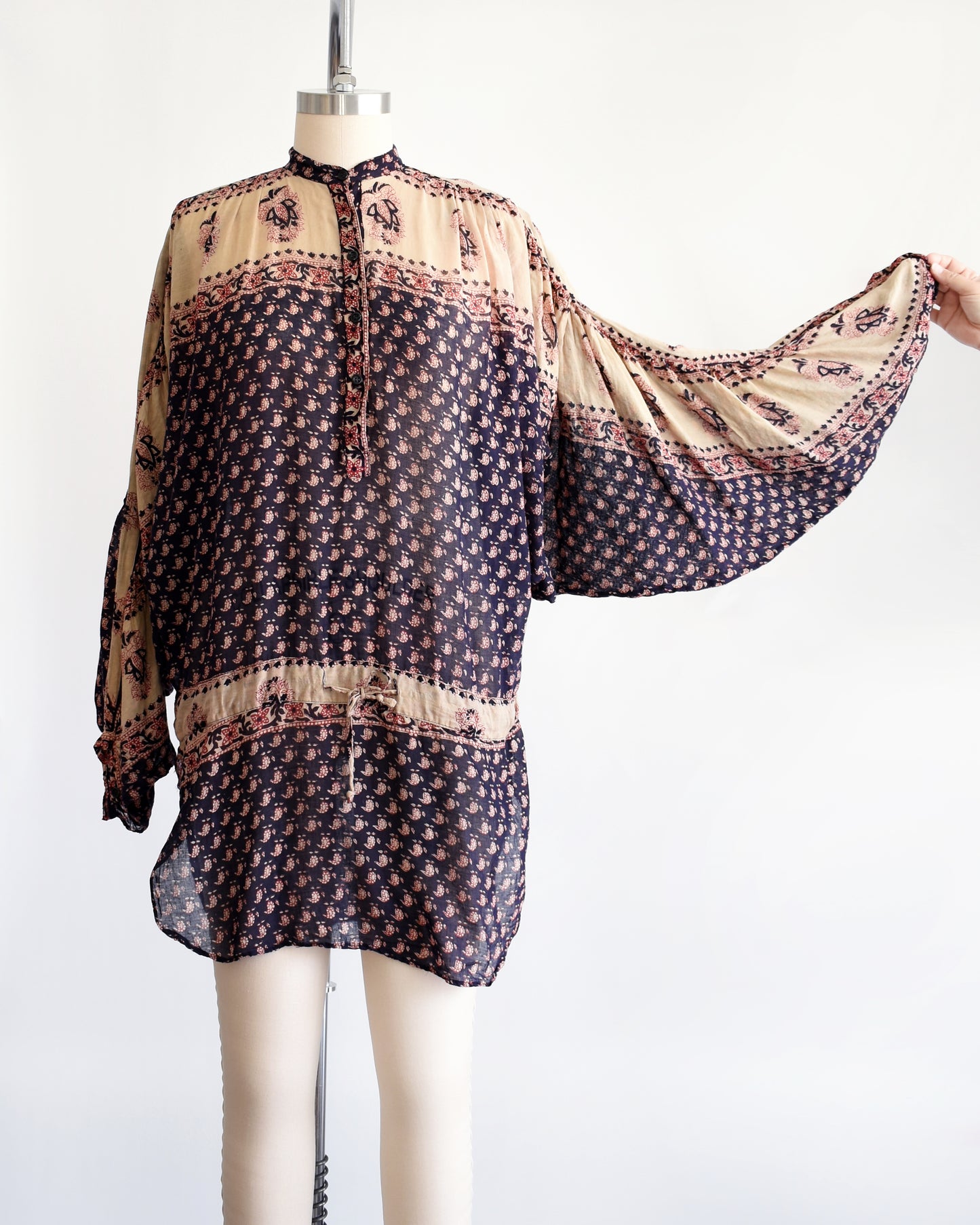 A vintage 1970s Indian cotton tunic made from thin, gauzy navy blue and light tan cotton with a red and navy floral block print. The top has large dolman balloon style sleeves which are shown