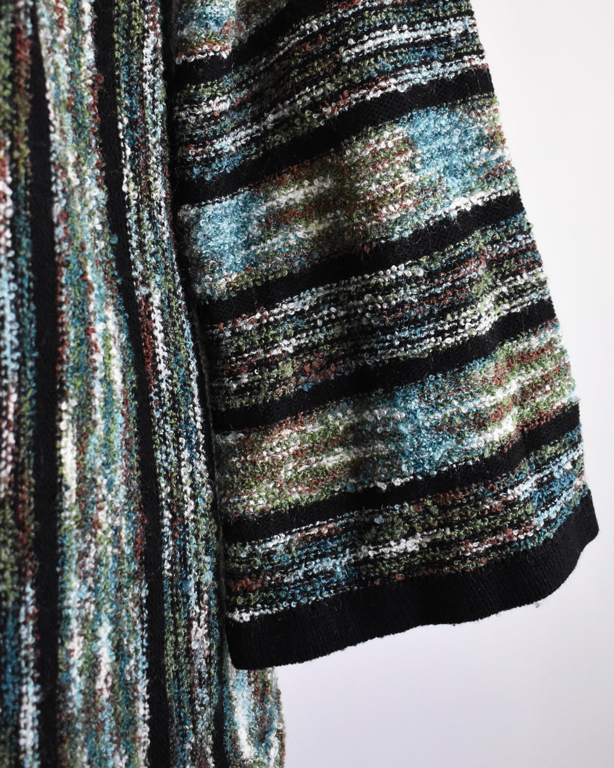 close up of the sleeves on a vintage 1970s open-front cardigan with wide bell sleeves, featuring a textured vertical stripe pattern in black, green, and white, displayed on a white dress form mannequin.