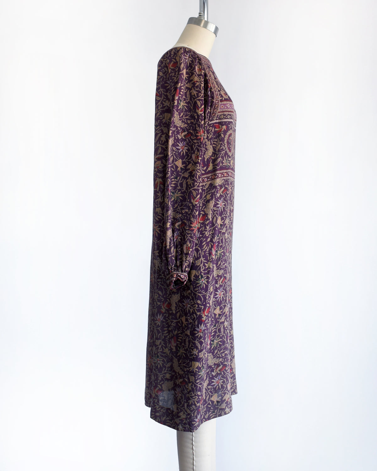 side view of A vintage 1980s long-sleeve knee-length dress with an intricate bohemian-style floral and bird print, displayed on a cream mannequin against a white background.