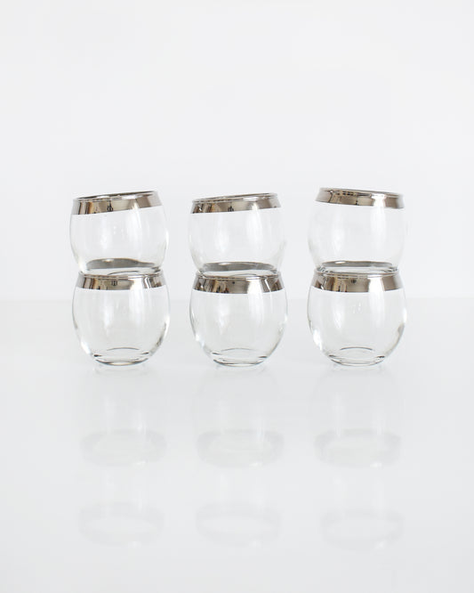 A row of six vintage silver rim roly poly shot glasses stacked in two in a row of three
