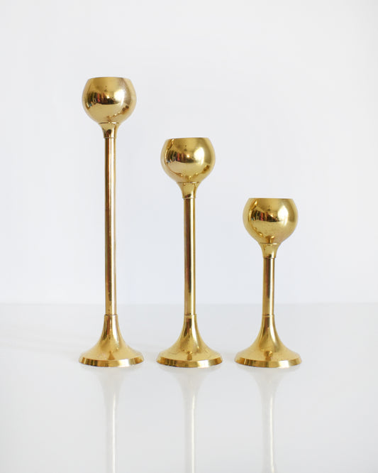 Set of three of vintage brass graduated candlesticks that have rounded tapered tulip shaped holders, thin stems, and a round base.