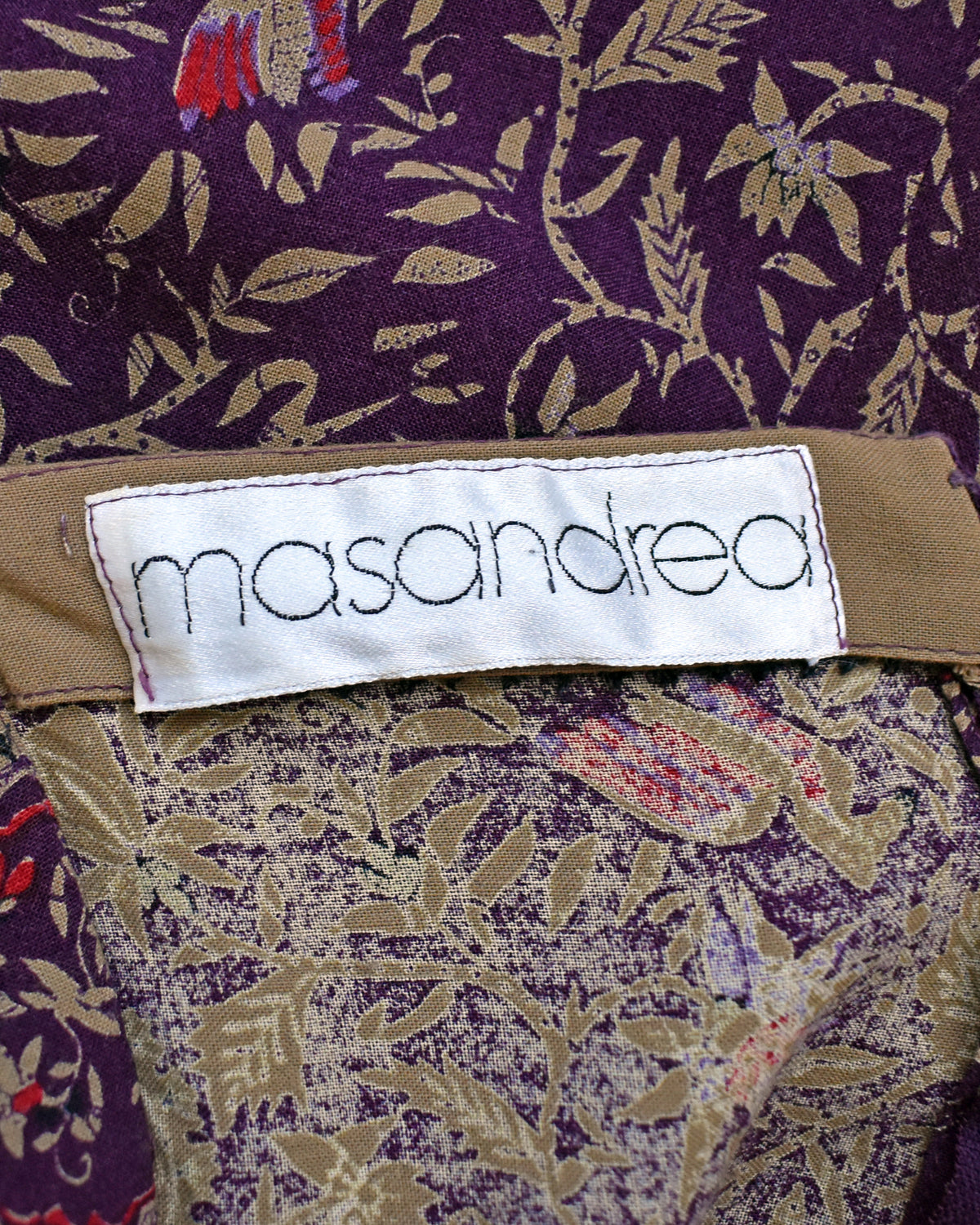Close-up of a garment label reading 'masandrea' sewn onto a patterned fabric with purple, beige, and red floral motifs.