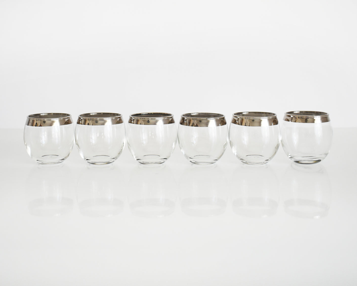 A row of six vintage silver rim roly poly shot glasses in a row