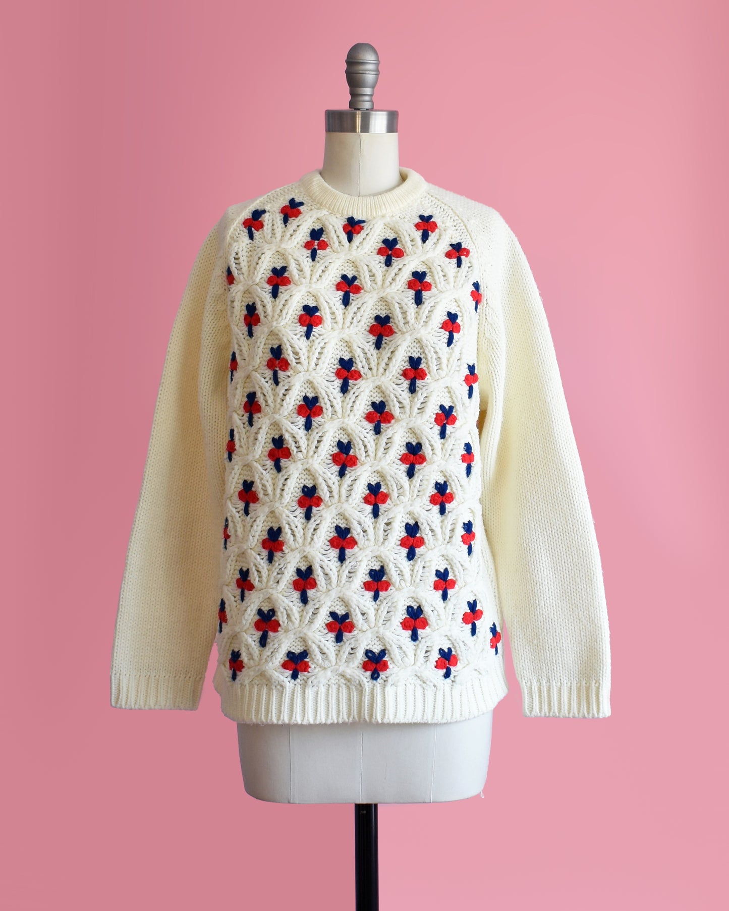  a vintage 1970s white sweater with red and blue floral pattern on a mannequin against a pink background