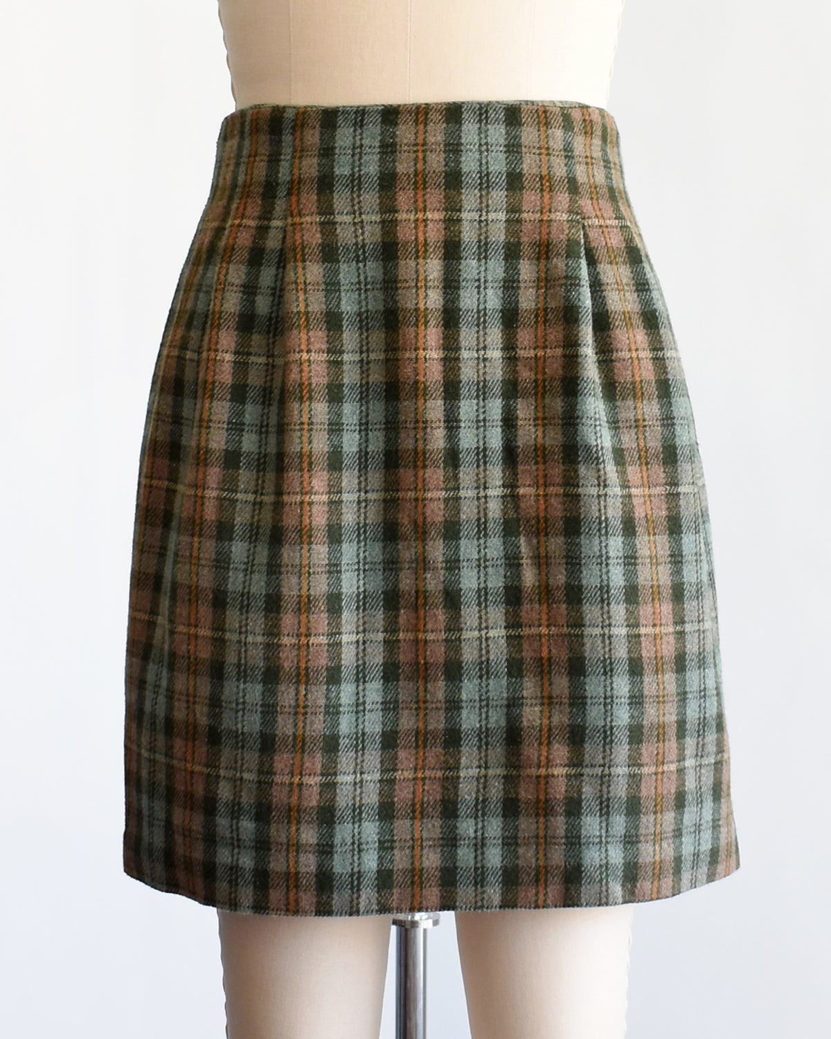A vintage 1990s  green plaid mini skirt in green, brown, and beige tones, displayed on a cream-colored dress form mannequin against a plain white background.