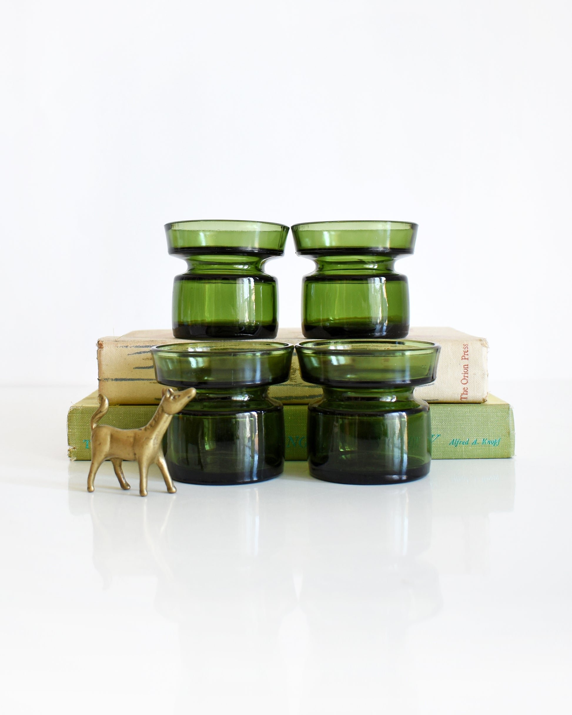 Set of four vintage 1960s green glass  Dansk candle holders. Two of the glasses are on a book and a small brass horse is to the left.