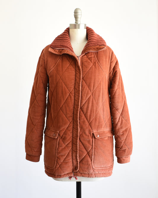 A vintage 1970s rust-orange quilted corduroy jacket displayed on a cream dress form mannequin against a plain white background.